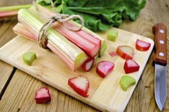 Bundle of stalks rhubarb, cut pieces of rhubarb with a sheet and a knife on a wooden boards