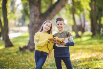 Happy Caucasian siblings enjoying in autumn day in park, sunny weather. Kids having fun holding