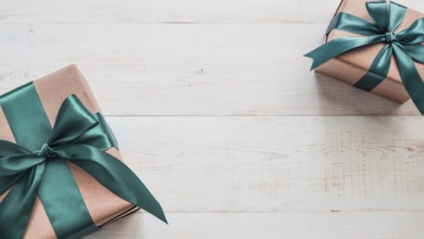 Two gift boxes in craft wrapping paper and green satin ribbon on white wooden table, copy space in