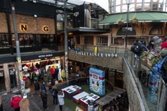 Shoppers at an elevated outdoor market with clothing stores and signs in the London Borough of