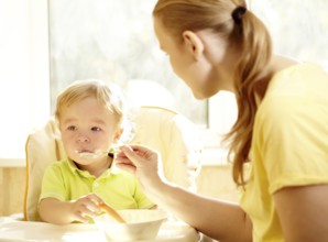 Young mother is feeding her two year old boy with porridge