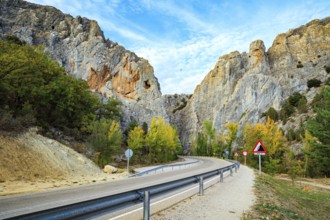 The trip to Spain. Asphalt highway passes among steep cliffs. The sky is covered with light clouds.