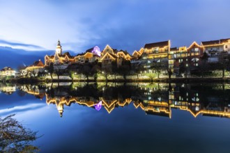 Christmas illuminated house facade of Frohnleiten reflected in the river Mur, blue hour,