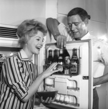 In the kitchen 1950s. A couple in their kitchen and at the refrigerator where the beer is kept in