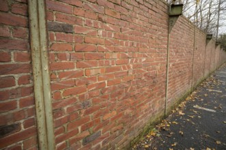 Red brick wall with metal supports and fallen autumn leaves on the ground beside a paved area