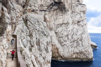 Two women walking on staircase amidst Capo Caccia cliffs. Alghero, Sardinia. Italy