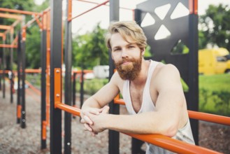 Portrait young bearded man standing on public sports ground and training on parallel bars. Handsome