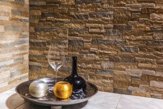 Still-life with a black glass jug, a transparent glass and two candlesticks. Background stone wall.