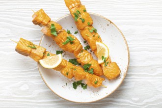 Grilled barbecue salmon skewers seasoned with green parsley and lemon on ceramic plate on white