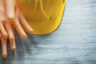 Pair of rubber insulating gloves building helmet on wooden board electricity concept