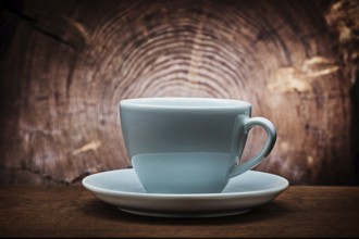 Big white coffee cup for capuchino on vintage wood background with cross cut of tree trunk