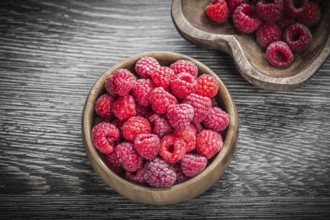 Round and heart-shaped bowls with ripe raspberries on wooden board