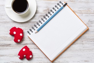 Coffee cup notepad pencil and two red hearts on wooden surface