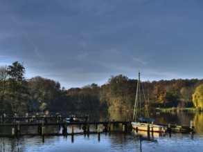 Several boats on a calm autumn lake, framed by trees and jetties, under a blue sky, Borken,
