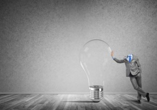 Headless businessman in empty room leaning on glass light bulb