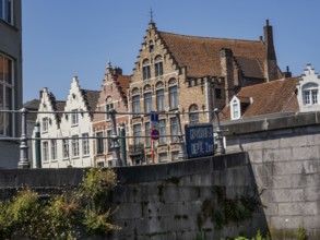 Historic brick buildings along a canal with a railing in the foreground and blue sky, Bruges,