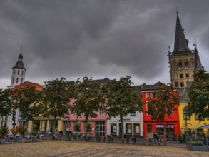 Colourful houses on the market square with a church and church towers in the background under a