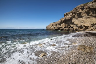 Empty pebble tropical beach under white cliffs against blue sky. Copy space
