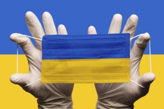 Doctor holding in white gloves protection medical face mask with National flag of Ukraine