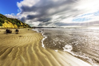 New Zealand. Moeraki's huge round boulders on a sandy beach. The Pacific ocean tide begins. The