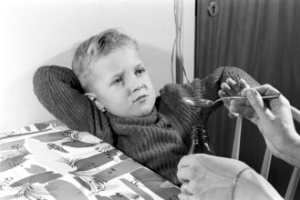 A boy is sick and won't take his medicine. His mother holds out a spoon and waits for him to gape