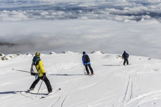 Three free riders are prepairing for skiing down a snowy rocky mountain top