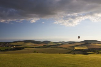 Hot air balloon flying over a golf course and amazing valley at sunset