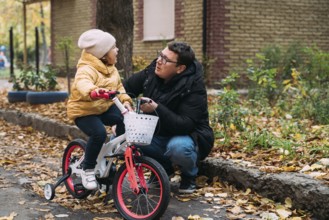 Father with daughter learning to ride the bike. Autumn weekend day in the city neighbourhood.