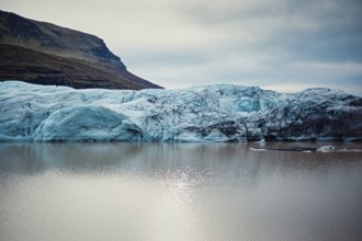 Massive blue glacier reflecting in a calm lake surrounded by rocky mountains, iceberg, glacier,