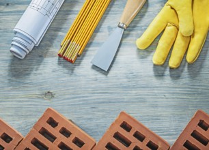 Assortment of red bricks safety gloves palette knife blueprints wooden meter building concept