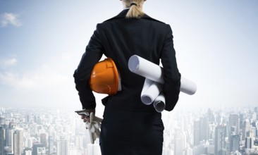 Woman architect standing with construction drawings and hardhat in hands. Back view of contractor