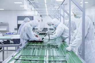 Factory workers in white lab suits and face masks, producing tv sets on a green assembly line with