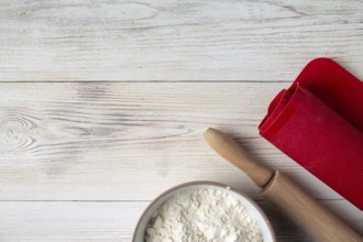 Cup with flour, rolling pin, cooking mat on wooden table, copy space