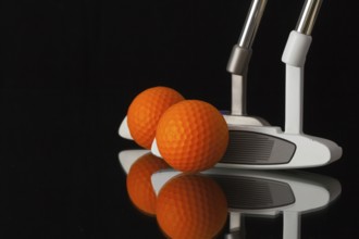 Two different golf putters and balls on a black glass desk