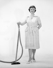 Cleaning day in the 1960s. A woman is standing holding a vacuum cleaner, looking happy. Sweden