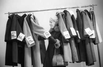 Great discounts of outerwear in the 1960s. A woman stands by a clothes rack, choosing from