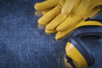 Noise reduction yellow headphones and leather protective gloves on scratched metallic background