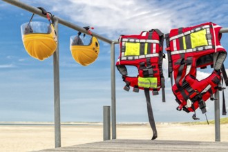 Safety helmets and life jackets hanging on railing near beach at coast