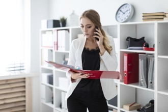 Beautiful young girl with blond hair in a white jacket and black blouse is working in the office.