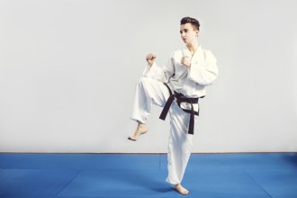Girl in karate suit kimono in studio at grey background. Female child shows judo or karate stans in