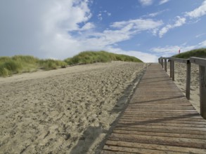 A long wooden walkway leads up sandy dunes, with a sky of clouds and blue, Juist, East Frisia,