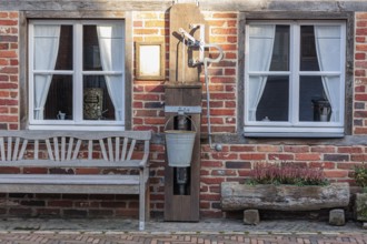 Rustic brick wall with two windows, old water pump and bench against a rural backdrop, gemen,