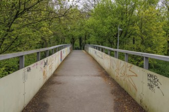 Pedestrian bridge with graffiti on the sides, surrounded by green trees, Rotterdam, Netherlands