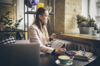 Woman sitting coffee shop wooden table, drinking coffee and using smartphone. Woman Using Phone In