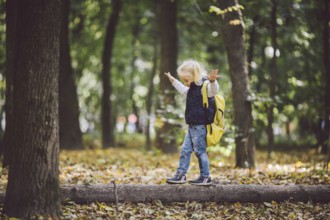 The theme children outdoor activities. Funny little baby Caucasian blond girl walks through forest