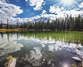 Small shallow lake surrounded by pine forest. The mirror surface of water reflects the cloudy sky.