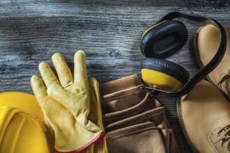 Leather protective gloves boots tool belt hard hat earmuffs on wooden board