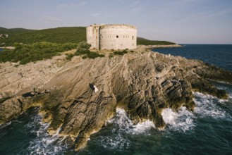 Bride and groom stand on the rocks near the fortress by the sea. Aerial view.