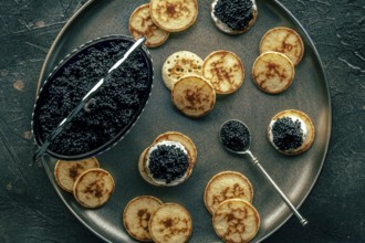 Blinis with caviar, overhead flat lay shot on a festive dish, mini pancakes, an elegant appetizer,