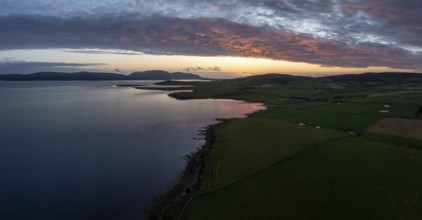 Sunset with cloud band on the coast of Scapa Flow with view to the island of Hoy, drone shot,